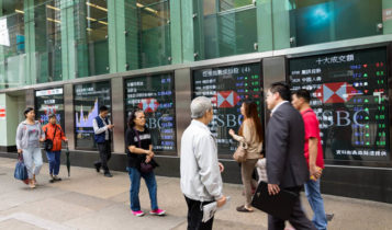 Asian shares are shown on electronic boards as people are walking by